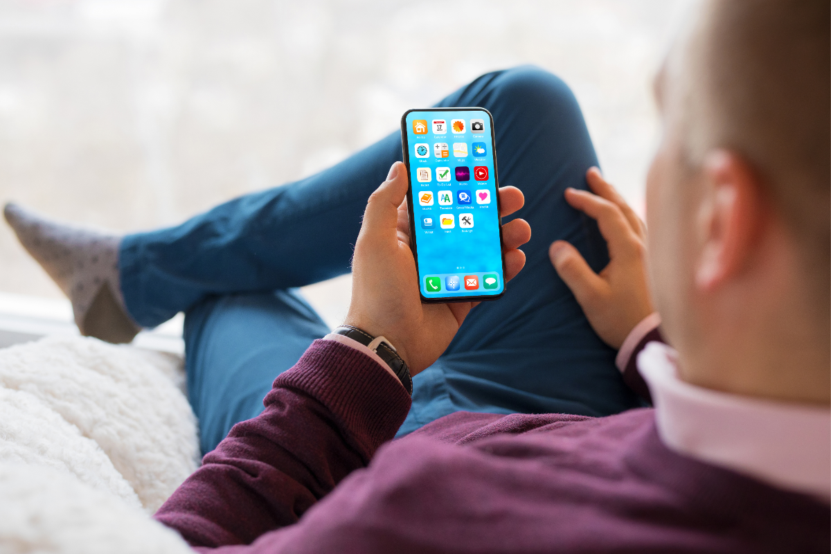A person sitting comfortably with legs crossed, holding a smartphone displaying a screen full of various colorful app icons, suggesting the potential of earning revenue through Android app development.