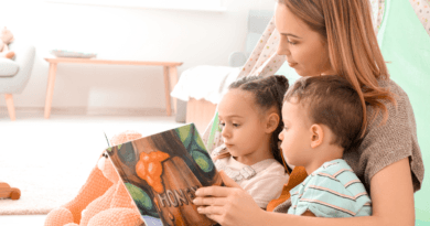 A warm and intimate scene of a young woman reading a children's book titled 'HONEY' to two attentive children, a girl and a boy, who are sitting close to her in a cozy home environment, with soft toys and a comfortable play tent in the background.