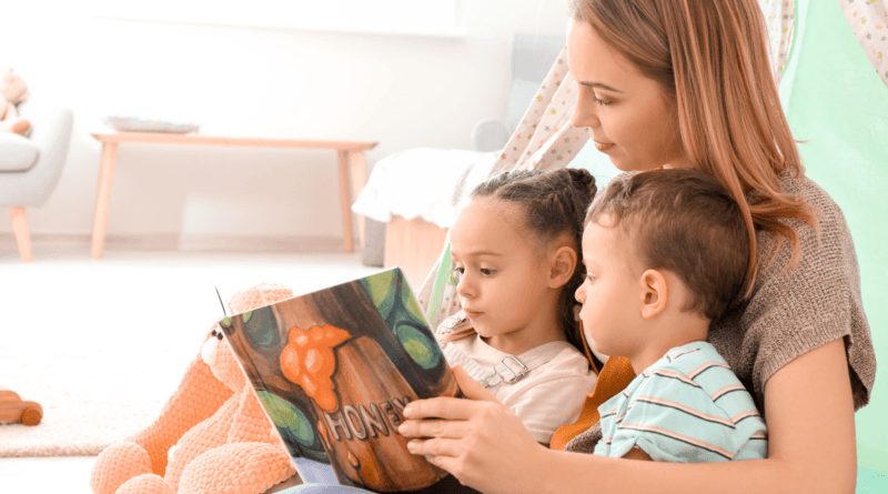 A warm and intimate scene of a young woman reading a children's book titled 'HONEY' to two attentive children, a girl and a boy, who are sitting close to her in a cozy home environment, with soft toys and a comfortable play tent in the background.