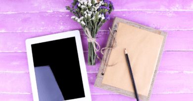 A digital tablet with a blank screen next to a pencil and notepad on a rustic burlap cloth, with a bouquet of white and purple flowers, all set against a vibrant purple wooden background, symbolizing the concept of making money by writing eBooks.